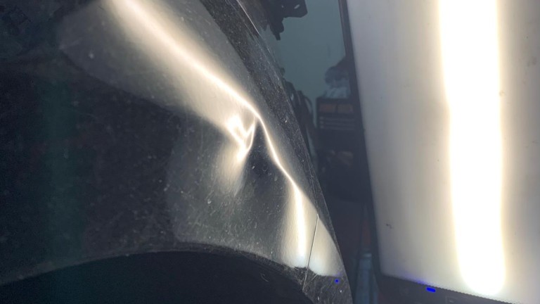 Schwere Delle im schwarzen Lack des rechten vorderen Kotflügels.